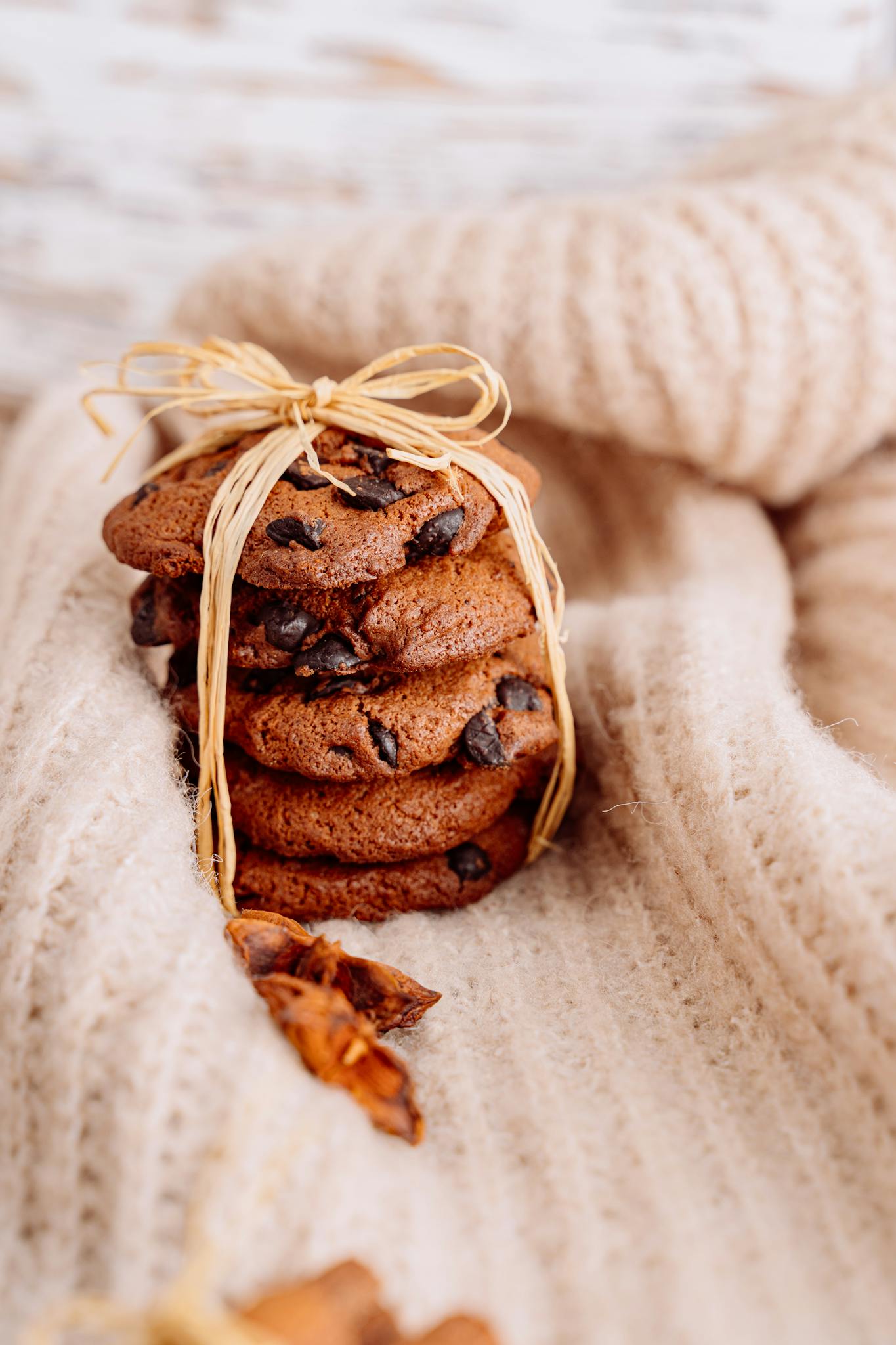 Warm stack of chocolate chip cookies tied with twine on a cozy knitted blanket